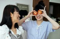 Happy Asian females in aprons entertaining with tomatoes while cooking together in kitchen