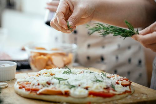 Free Crop anonymous person sprinkling green rosemary on pizza with cheese and tomatoes at table Stock Photo