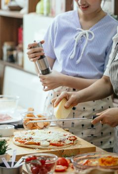 Crop anonymous females grating cheese on pizza placed on wooden board while cooking together in kitchen