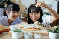 Cheerful ethnic women seasoning pizza with spices