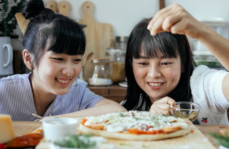 Smiling Ethnic Women Adding Condiments On Pizza