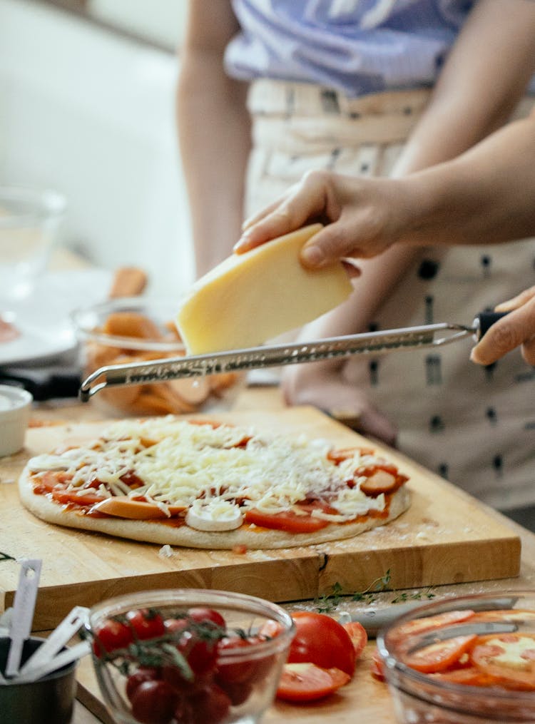 Anonymous Person Grating Cheese On Pizza