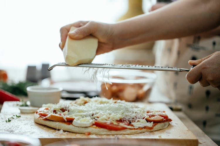 Anonymous Person Grating Cheese On Pizza