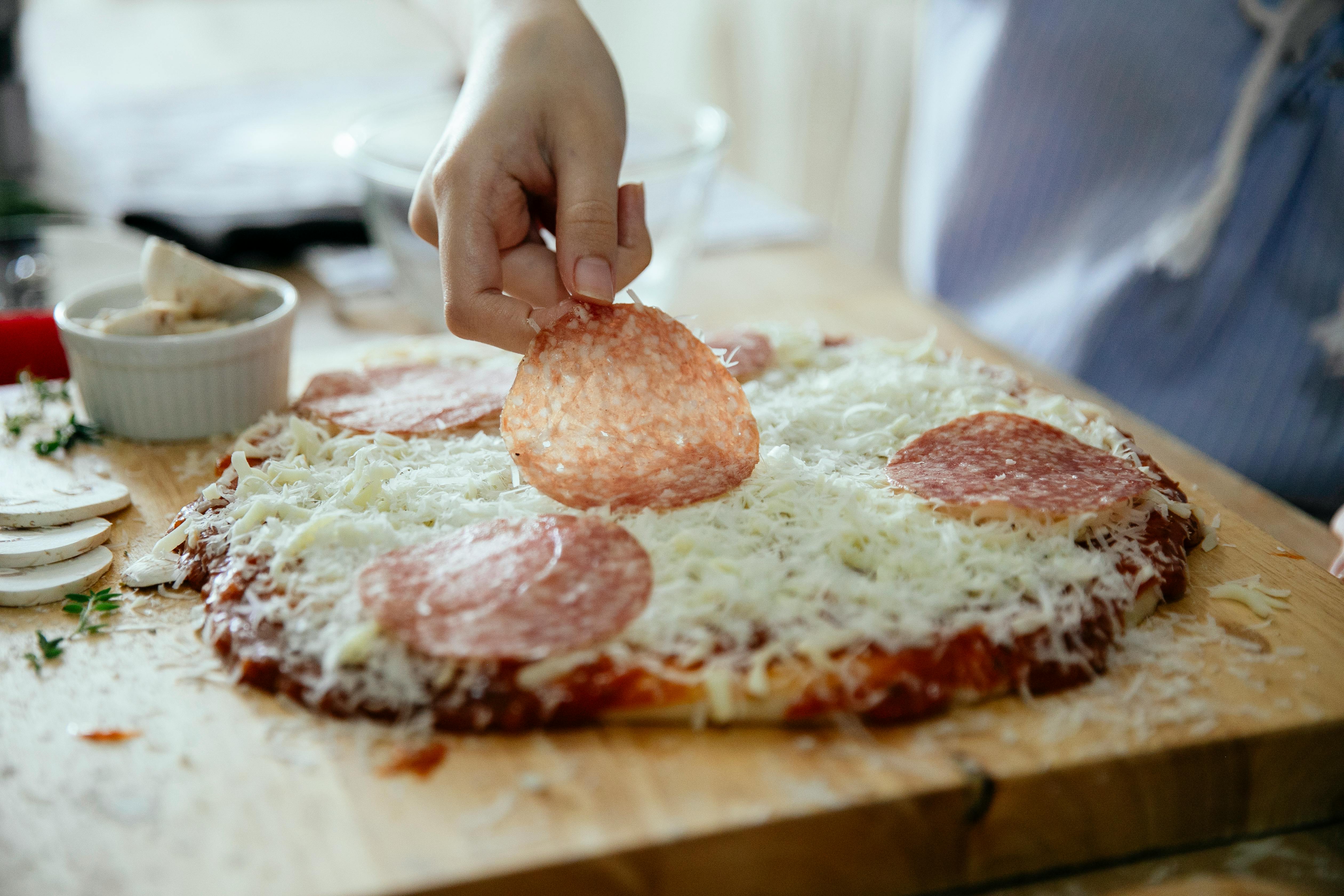 unrecognizable person adding salami in pizza