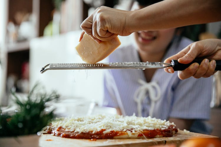 Woman Grating Cheese On Pizza