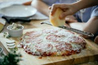 Unrecognizable person grating cheese on pizza