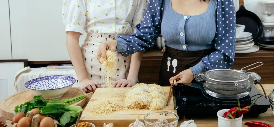 Ribbons of pale yellow homemade gluten-free egg noodles dusted with potato starch, coiled into small nests on a wooden cutting board next to a rolling pin.