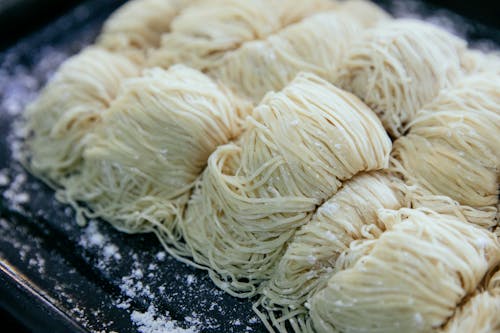 Homemade egg noodles collected in rolls and sprinkled with flour on black baking sheet