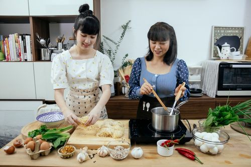 Free Smiling mother and daughter in casual wear and aprons cooking homemade noodles on kitchen table with cooking ingredients Stock Photo