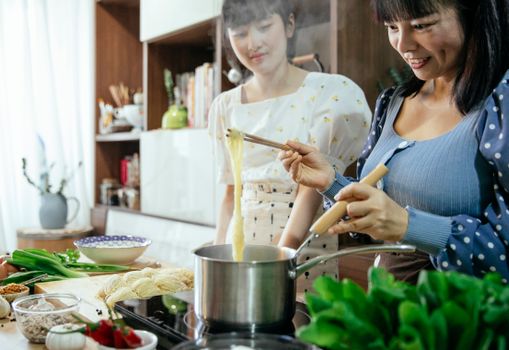 一对亚洲母女在舒适的厨房里一起煮面条，欢乐地展示着烹饪传统