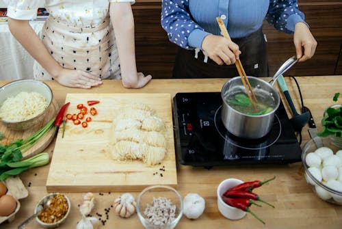 Free High angle of unrecognizable women boiling greens in saucepan making noodles with spices Stock Photo