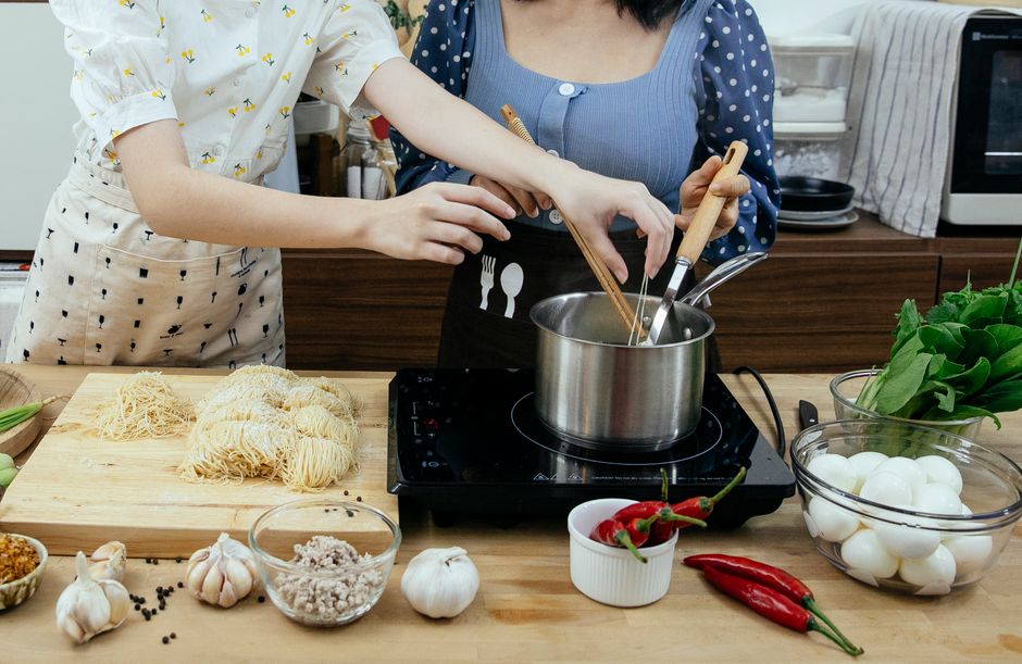 Photo by Katerina Holmes on Pexels Crop anonymous females in aprons boiling homemade noodles in saucepan on tabletop stove surrounded by fresh assorted ingredients in contemporary kitchen