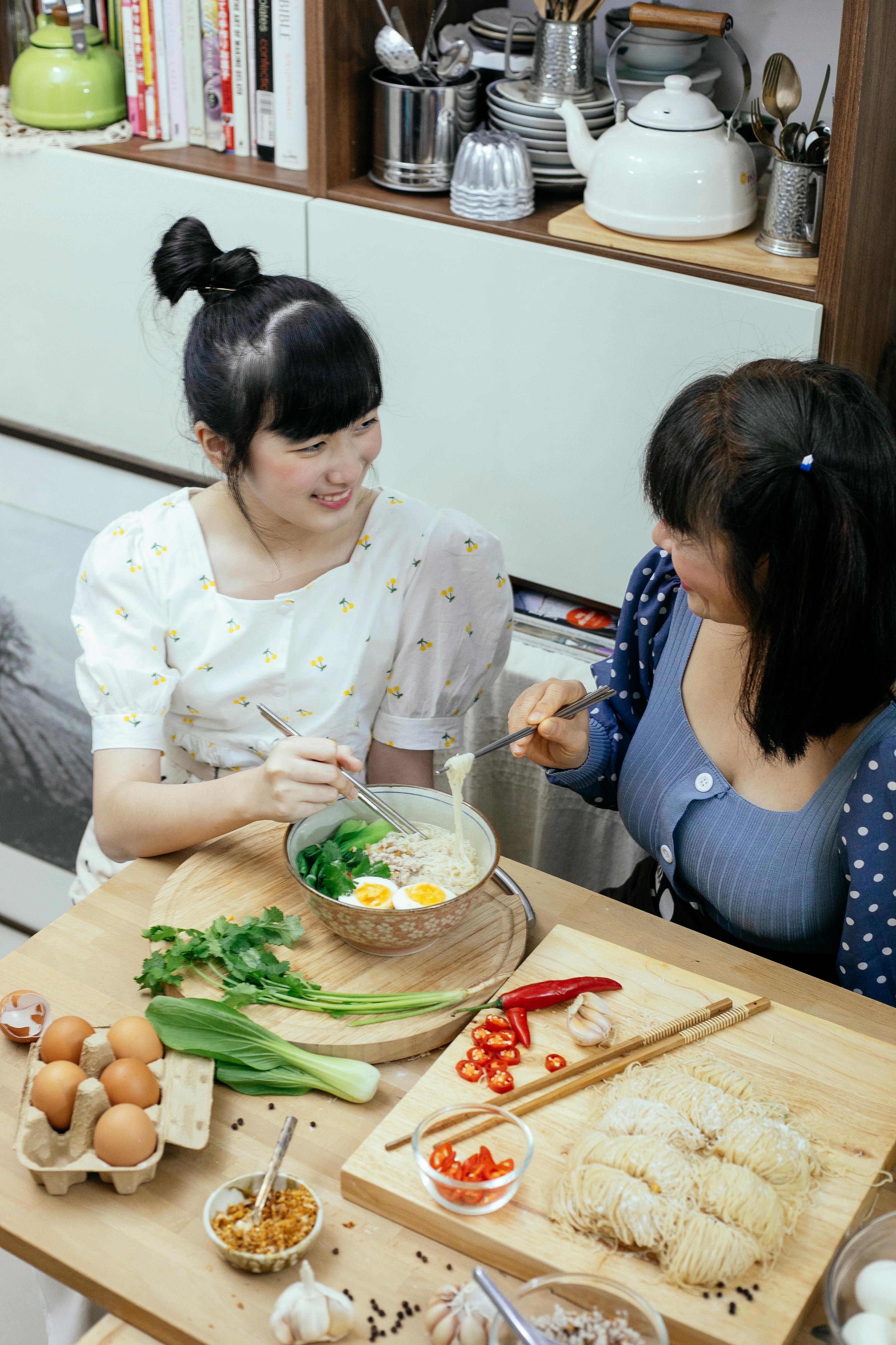 cheerful asian women eating tasty ramen soup and chatting