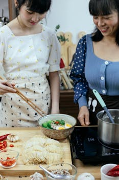 Two women enjoying cooking a delicious noodle dish in their kitchen.