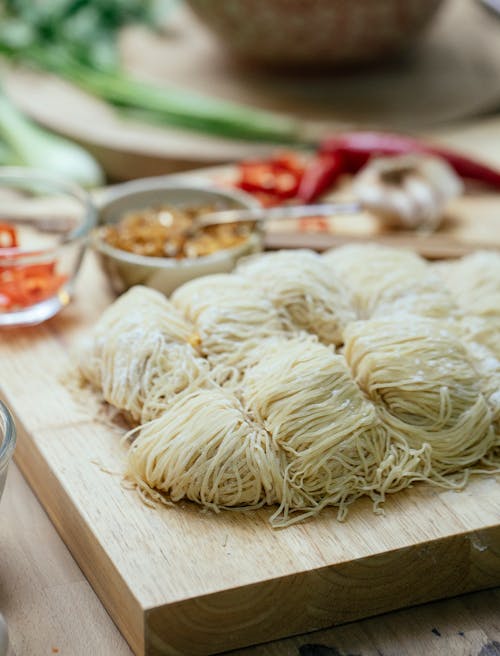 Composition of uncooked homemade pasta placed on wooden cutting board near fresh cut vegetables in light kitchen