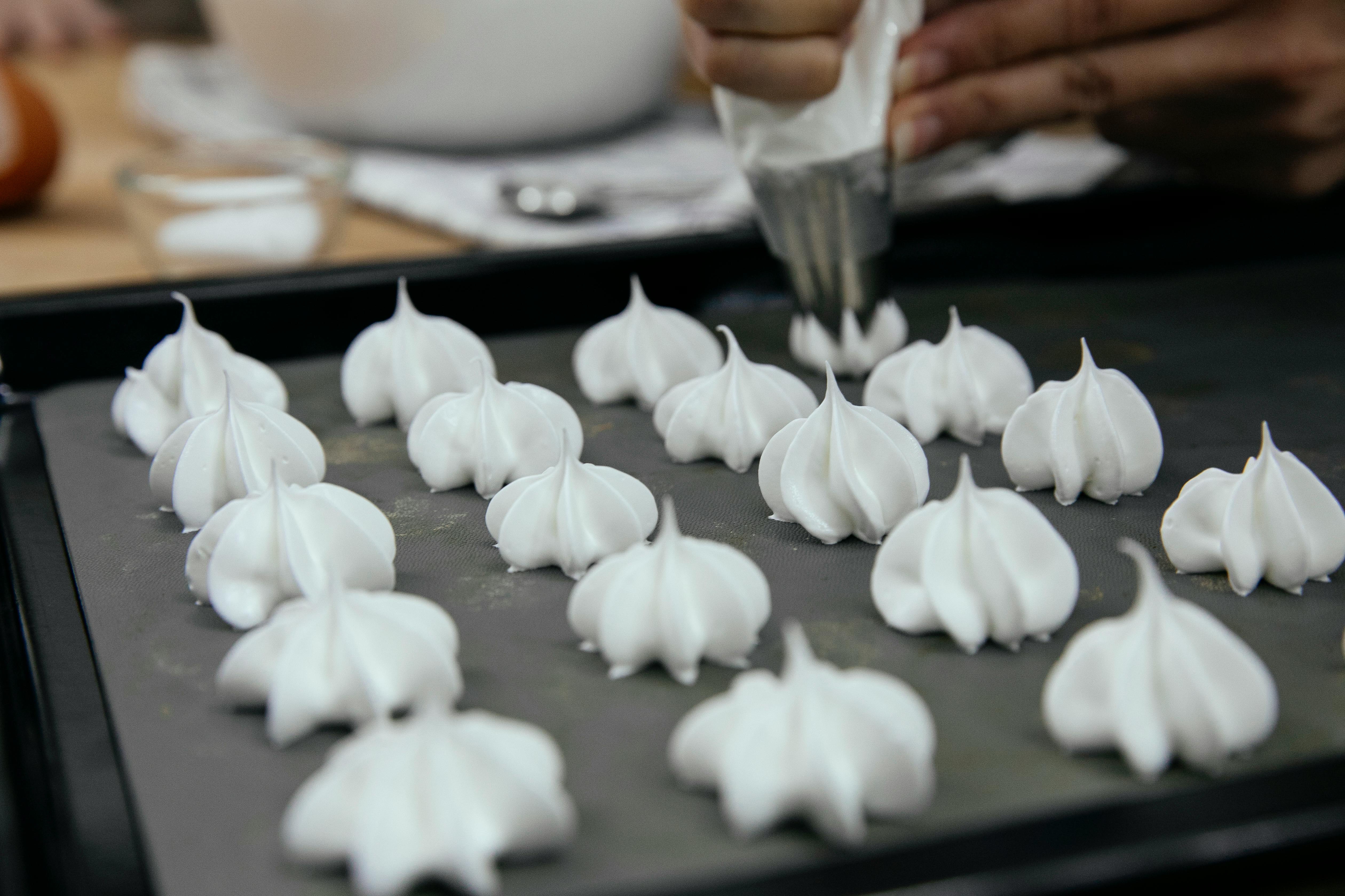 crop chef with piping bag forming meringues on baking pan