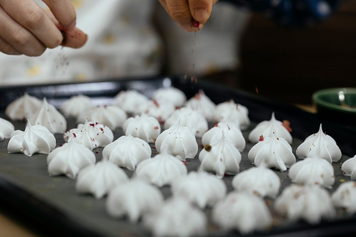 Crop anonymous chef pouring sweet chocolate powder on vanilla meringue cookies placed on baking pan in kitchen