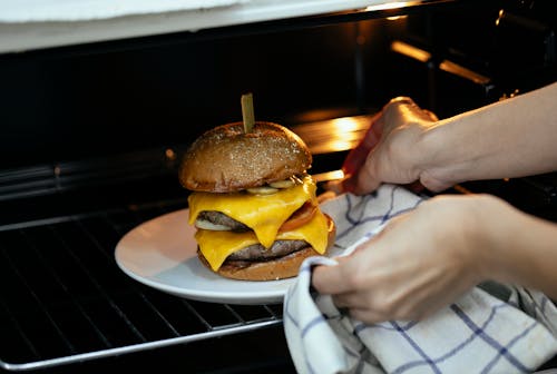 From above of unrecognizable person using towel to place burger served on plate in hot oven on rack while cooking