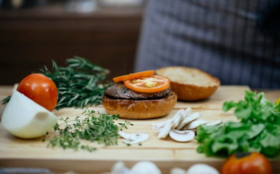 A close-up of a gourmet burger being prepared with fresh ingredients on a wooden board.