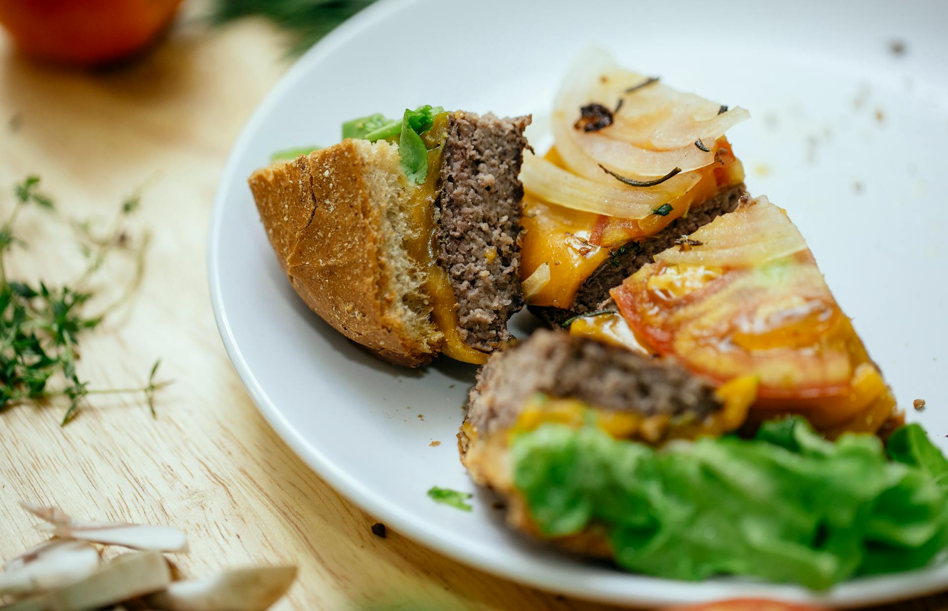 Delicious burger with juicy cutlet lettuce an onions cut into quarters served on white plate and placed on wooden table in kitchen against blurred background