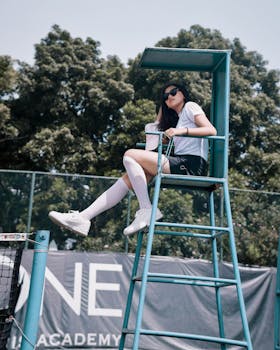 Young woman sitting on an umpire chair at a tennis court in Bandung, enjoying a sunny day.