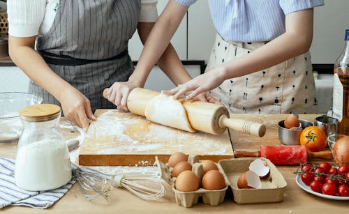 Crop women rolling dough on board