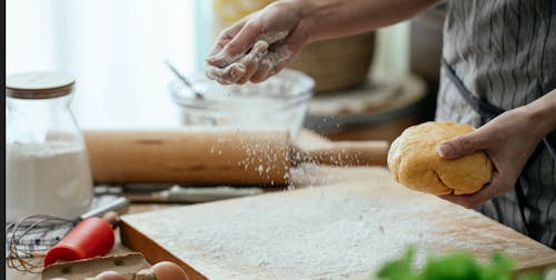 Free Unrecognizable female cook with ball of raw dough in hand spilling flour into wooden board while cooking in kitchen on blurred background Stock Photo