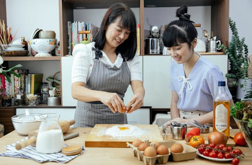 Asian mother and daughter smiling and baking together in a cozy home kitchen.