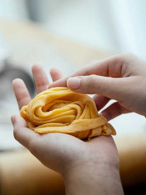 Free Unrecognizable cook with uncooked homemade pasta nest on hand standing near table on kitchen against blurred background while cooking delicious meal Stock Photo