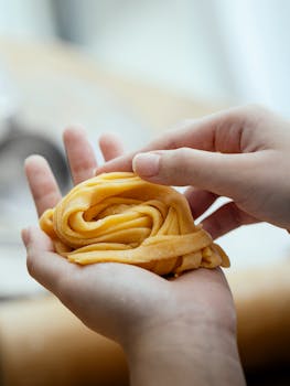 Unrecognizable cook with uncooked homemade pasta nest on hand standing near table on kitchen against blurred background while cooking delicious meal