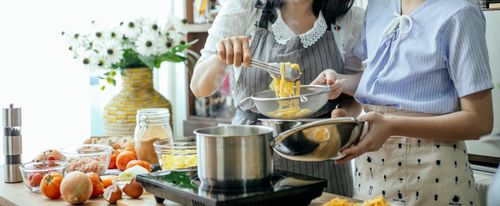 Free Unrecognizable female cooks putting pasta into sieve with tongs while standing near table with pan on stove and various ingredients while cooking lunch Stock Photo