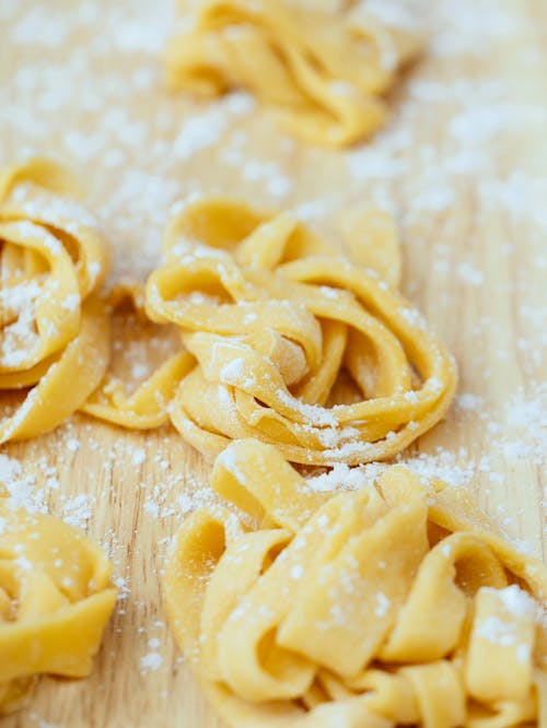 Closeup of fresh uncooked pasta with sprinkled flour placed on wooden board in kitchen during cooking preparation against blurred background