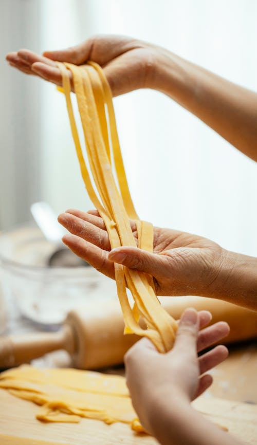 Free Unrecognizable cooks with uncooked pasta in hands standing at table in kitchen on blurred background while preparing dough for lunch Stock Photo