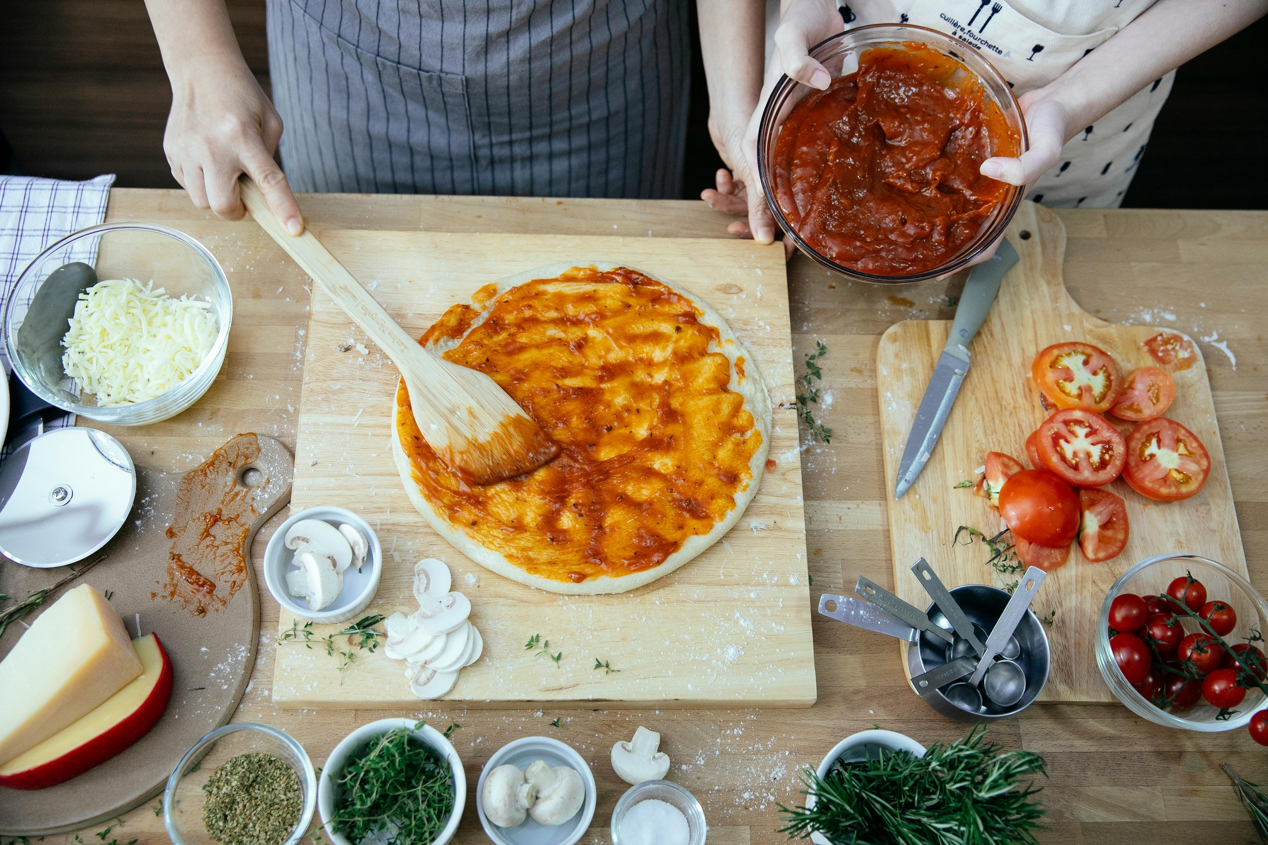 crop women spreading tomato sauce on pizza