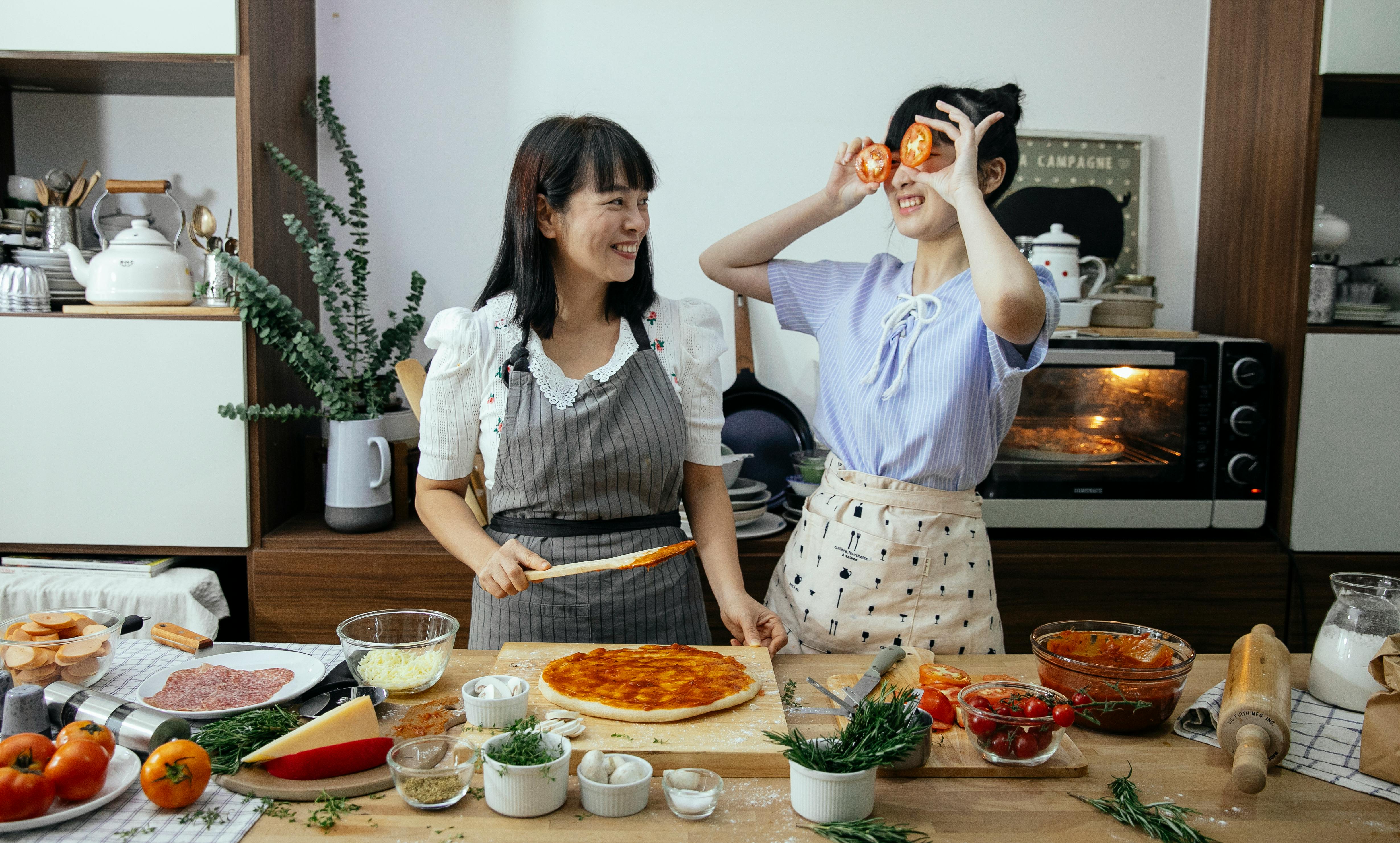 happy asian women putting sauce on pizza