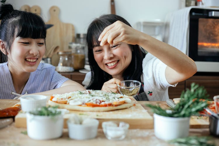 Cheerful Asian Women Sprinkling Seasoning On Pizza