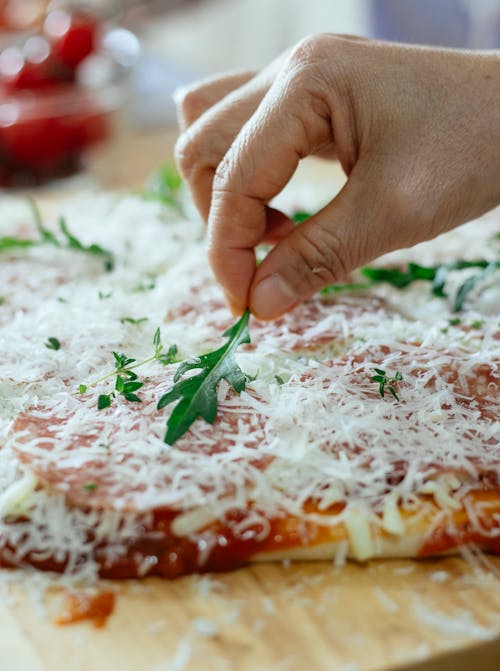 Crop person putting fresh herbs on pizza