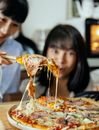 Positive blurred Asian women standing at table with tasty hot pizza with stretching cheese in kitchen while cooking together in lunch time