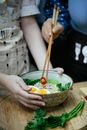 Unrecognizable female cooks with chopsticks putting chopped chili pepper in bowl with ramen topped with boiled eggs and greens during lunch
