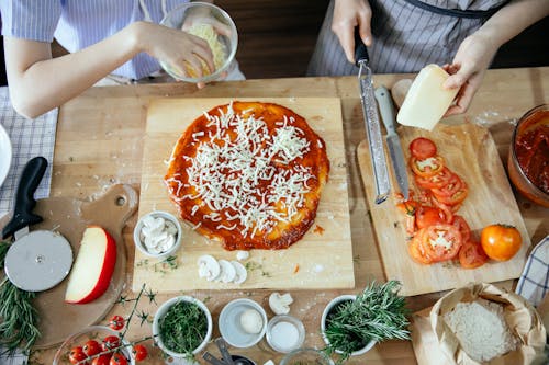 Crop women adding cheese on pizza