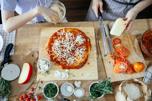 Crop women adding cheese on pizza
