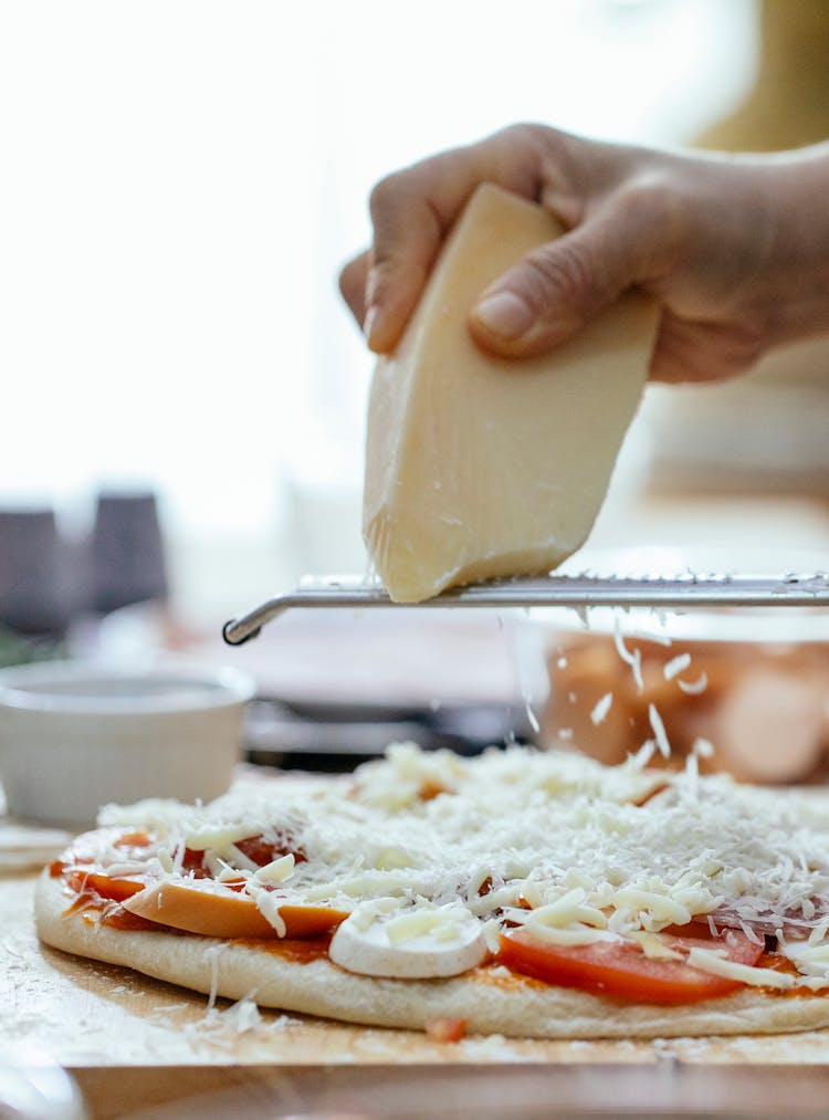 Crop Person With Grater Rubbing Cheese On Pizza