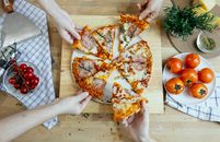 Crop friends taking slices of delicious pizza from cutting board