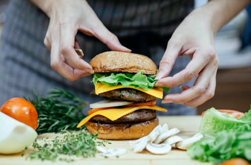 Free Crop anonymous female cook putting soft bread bun on top of lettuce leaves and meat patty while preparing double cheeseburger in kitchen Stock Photo