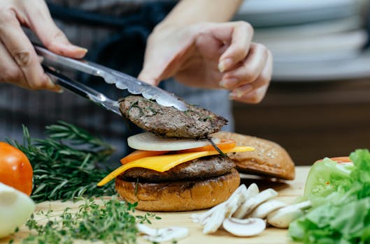 Chef arranging a gourmet cheeseburger with fresh ingredients on a wooden board.