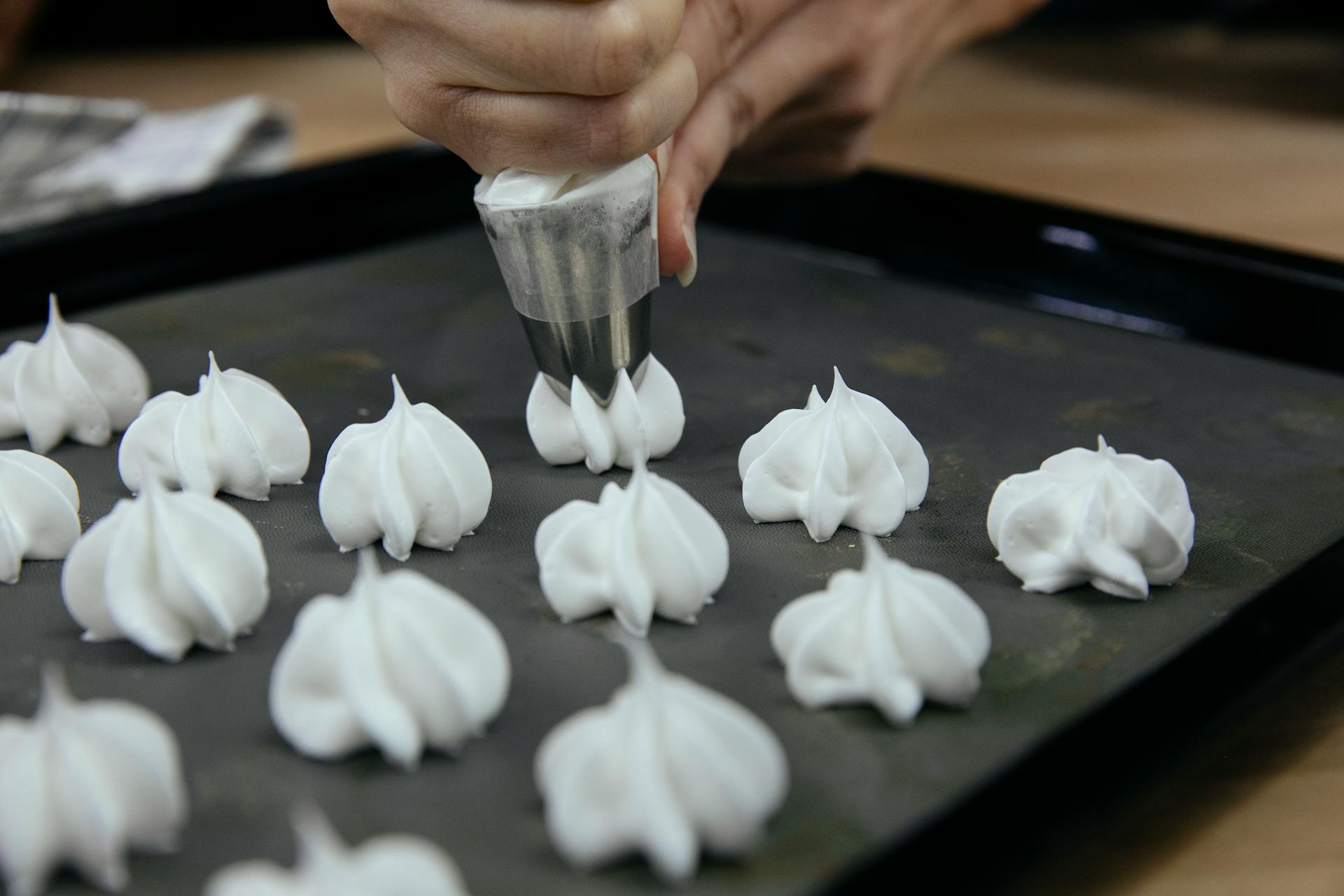 Crop anonymous cook putting out meringue from pastry bag onto baking tray during cooking process