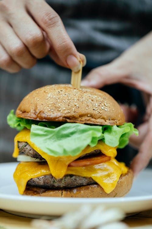 Crop cook inserting stick into delicious cheeseburger in kitchen