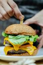 Crop cook inserting stick into delicious cheeseburger in kitchen