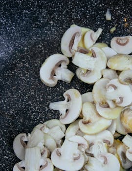 Top view of fresh white mushrooms in a nonstick frying pan, ready for cooking