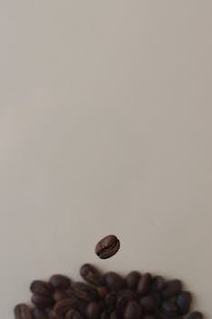 Minimalist image of a single coffee bean floating over a pile with soft focus.